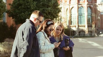 Three people looking at a smartphone outside a historic building