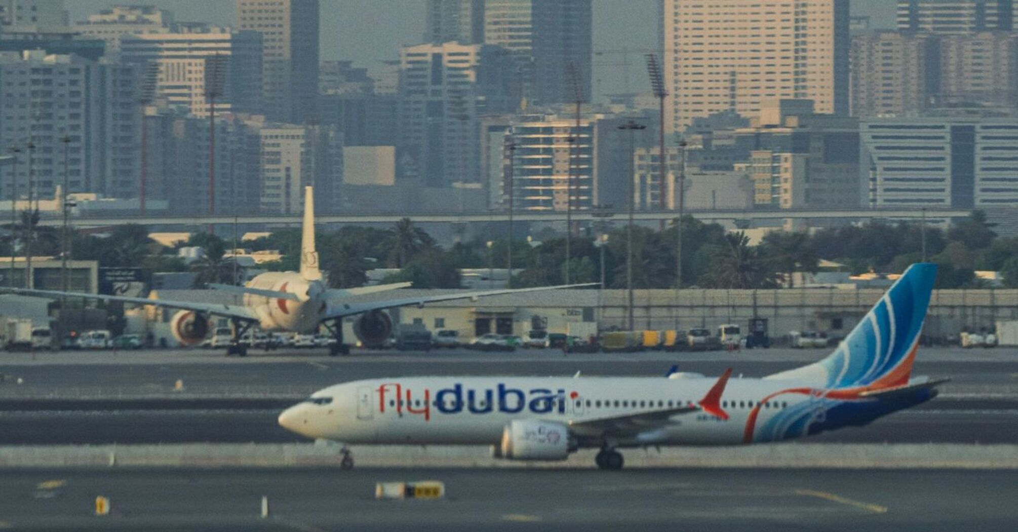 A flydubai aircraft taxiing on the runway with a city skyline in the background