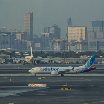 A flydubai aircraft taxiing on the runway with a city skyline in the background