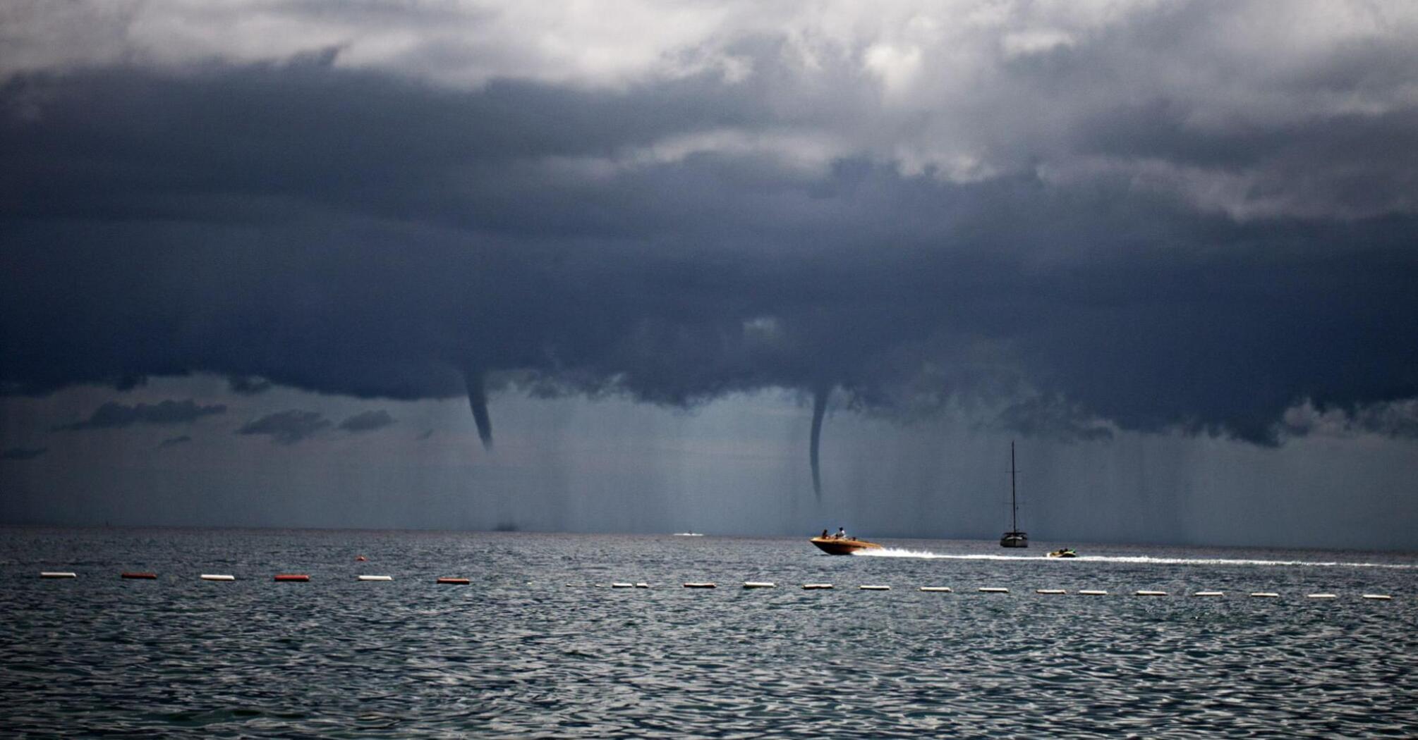 Dark storm clouds over the sea with two waterspouts forming near boats