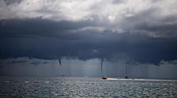 Dark storm clouds over the sea with two waterspouts forming near boats