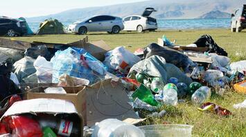 Trash scattered on grass near a lakeside camping area with cars and tents in the background