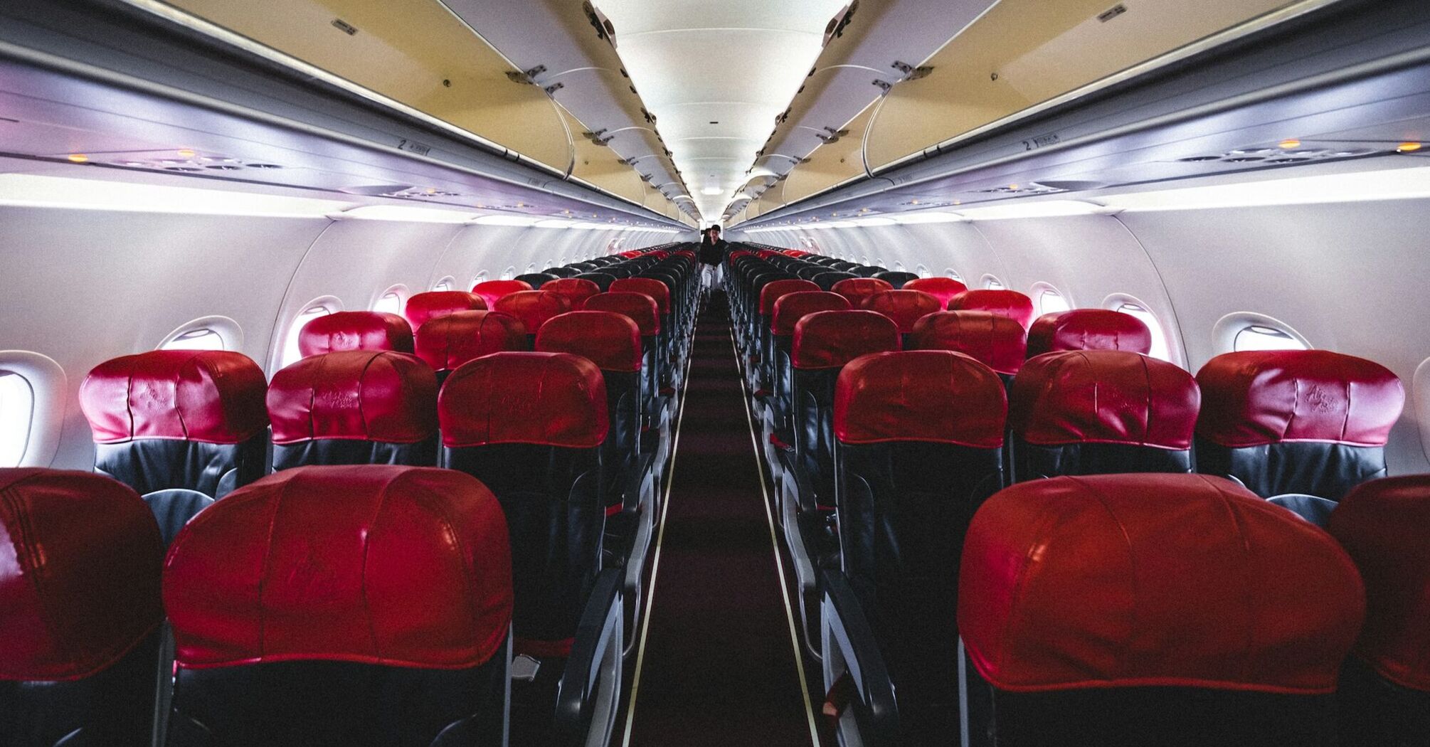 Interior view of an AirAsia airplane cabin with empty red seats lined up along both sides of the aisle