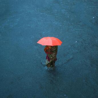 Woman with an umbrella wading through floodwaters