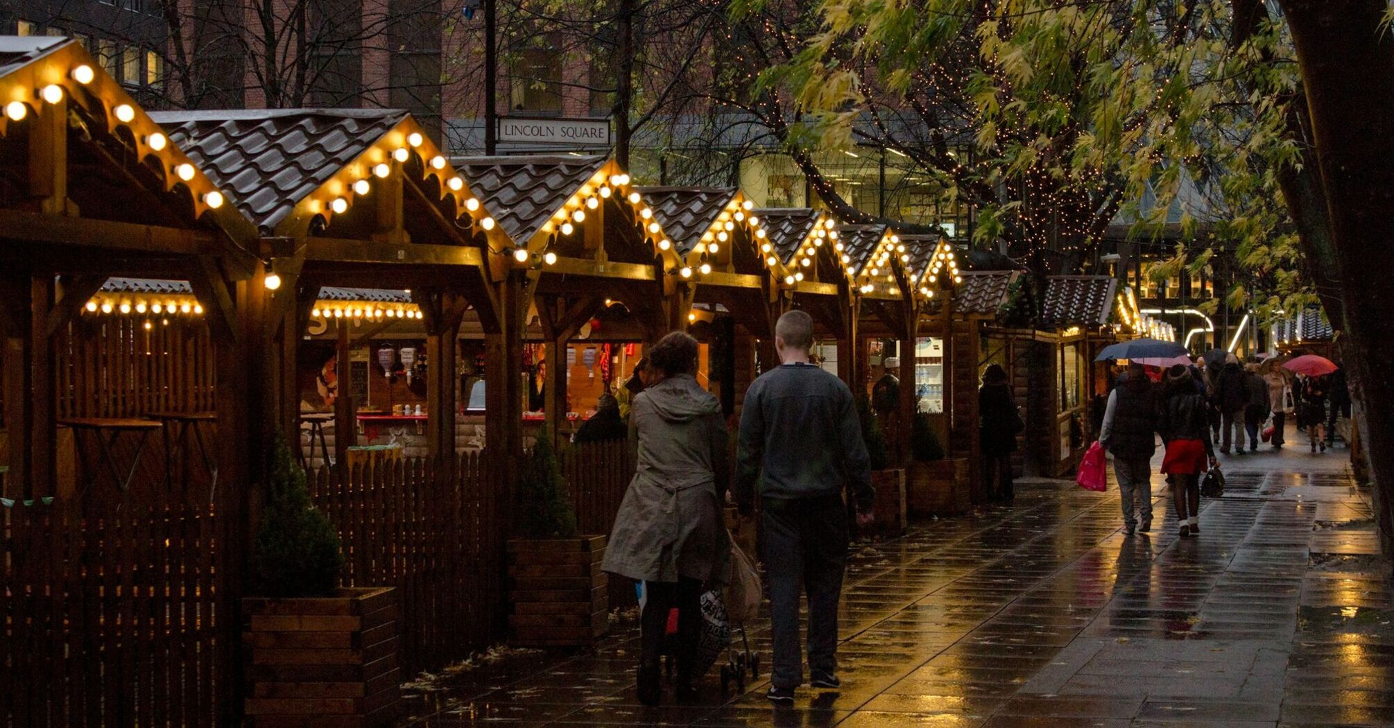 People walking along Manchester Christmas Market stalls on a rainy evening