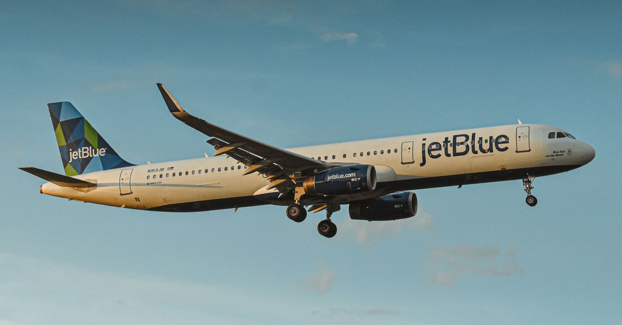 A JetBlue airplane flying in clear blue skies, showcasing the airline’s branding