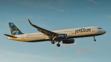 A JetBlue airplane flying in clear blue skies, showcasing the airline’s branding