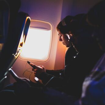 Airline passenger wearing headphones and using a phone during flight