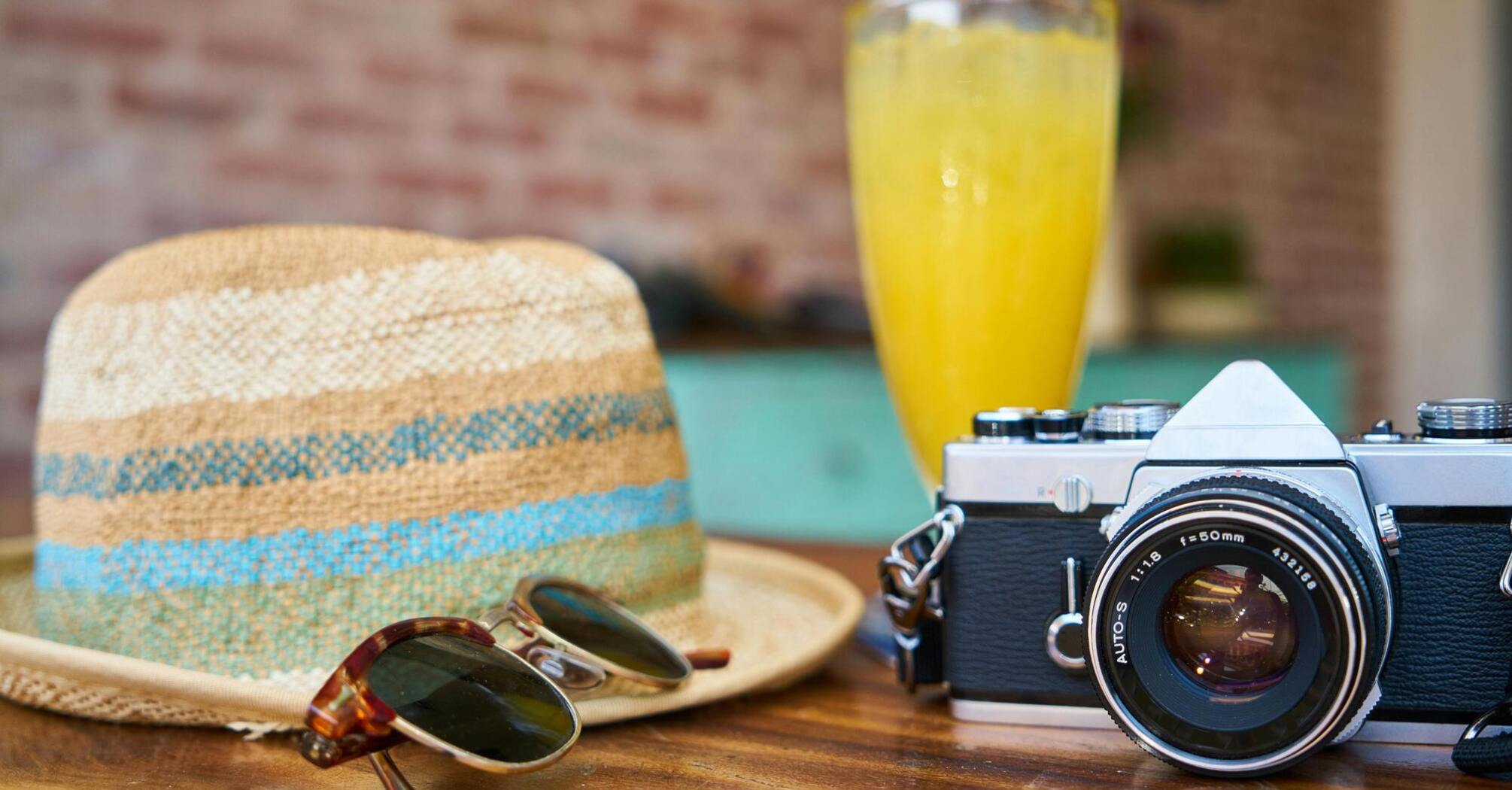 Straw hat, sunglasses, camera, and a refreshing drink on a table