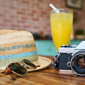 Straw hat, sunglasses, camera, and a refreshing drink on a table