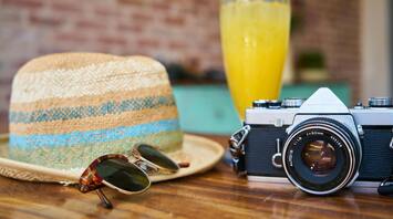 Straw hat, sunglasses, camera, and a refreshing drink on a table