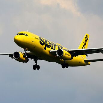 A Spirit Airlines yellow plane flying against a cloudy sky