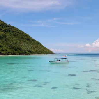 Boat floating on clear turquoise waters near a lush green island