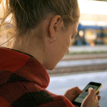 Woman checking train schedule on mobile phone at railway station