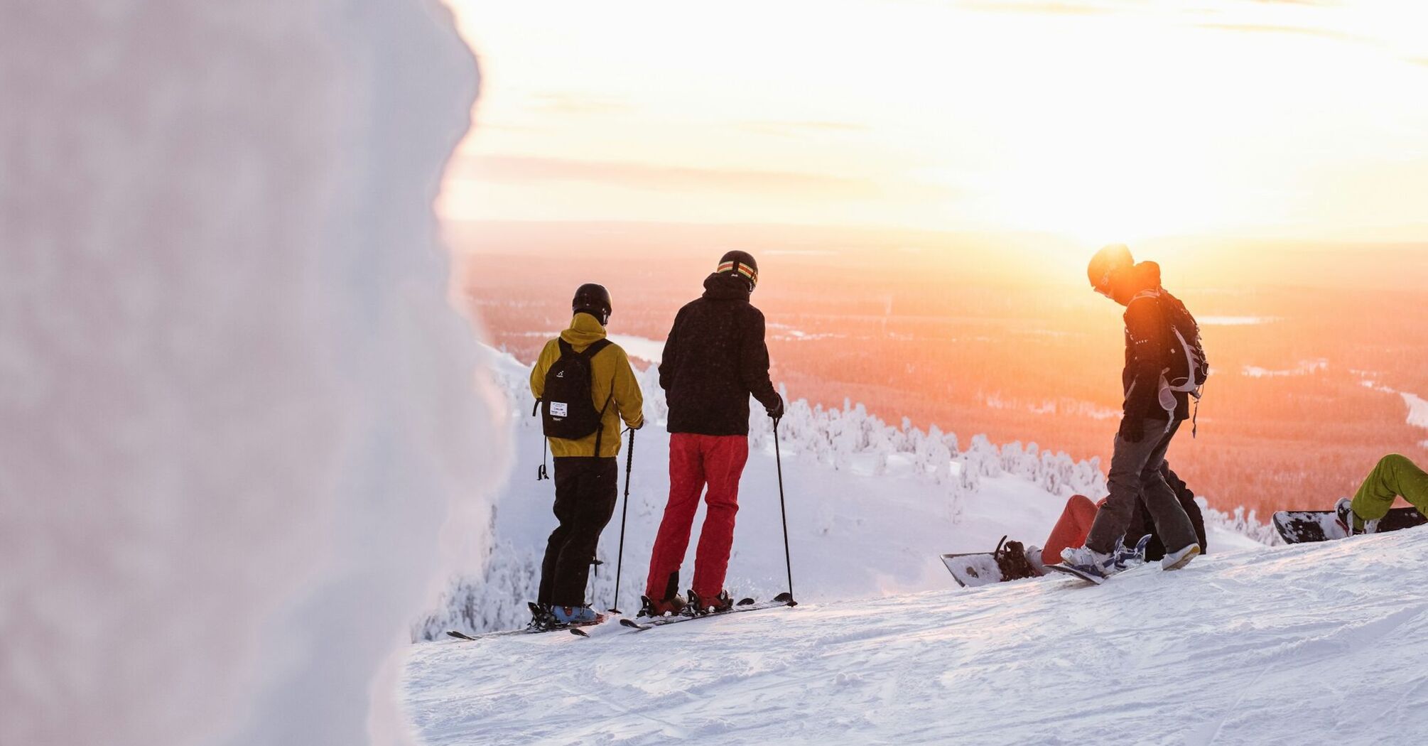 Skiers and snowboarder on a snowy slope with a sunset in Finland