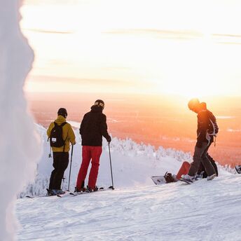 Skiers and snowboarder on a snowy slope with a sunset in Finland