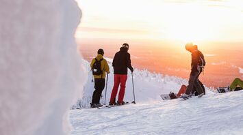 Skiers and snowboarder on a snowy slope with a sunset in Finland