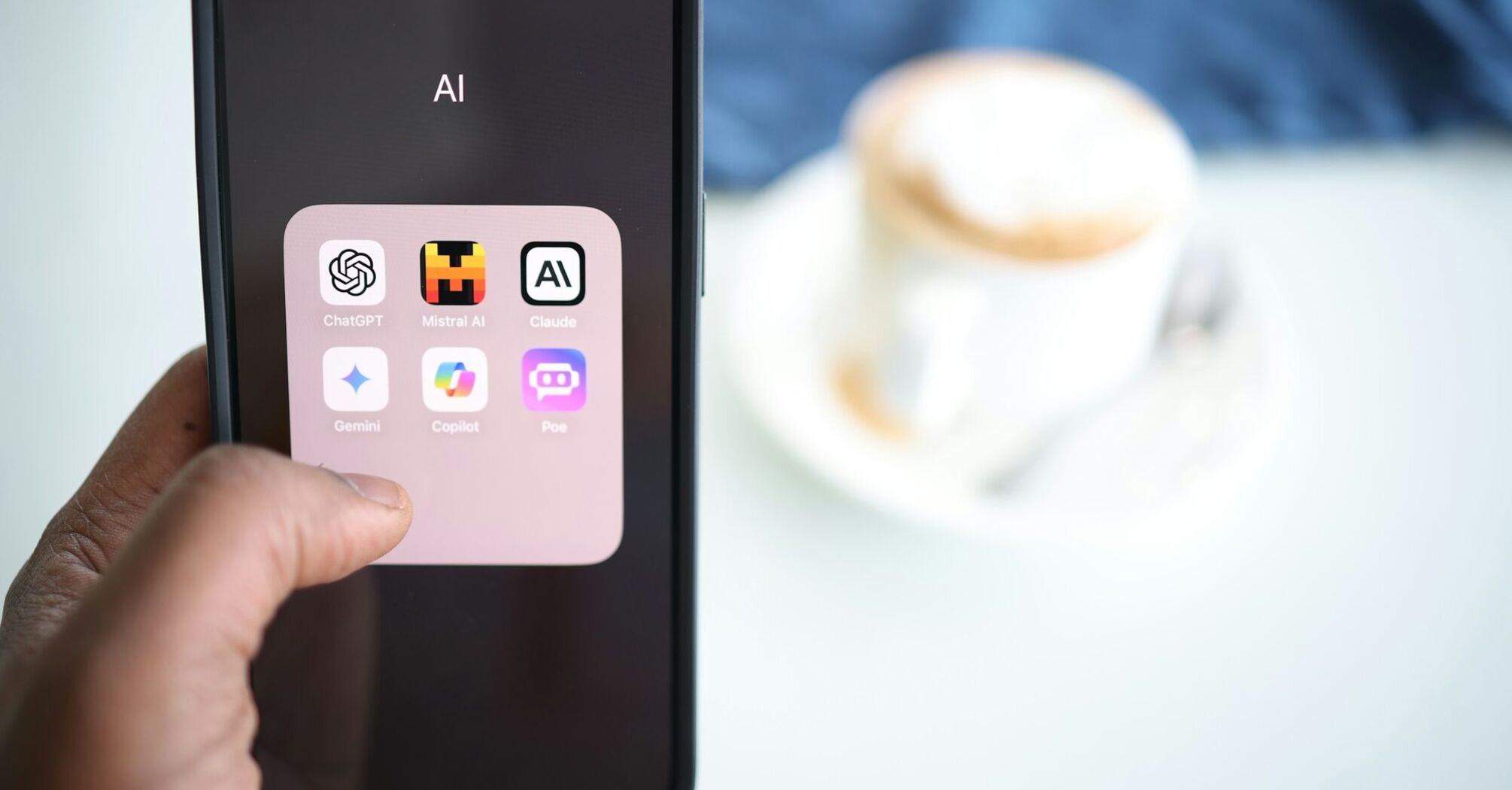 A smartphone screen displaying various AI applications, with a blurred background showing a cup of coffee