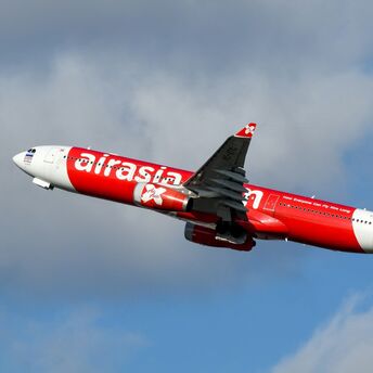 A red AirAsia plane in flight against a partly cloudy sky