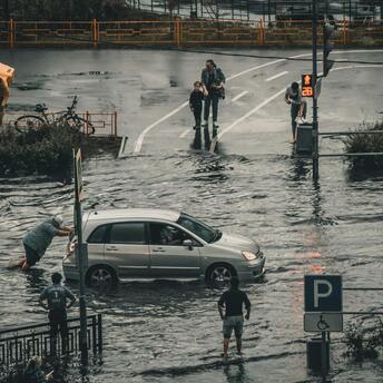 People navigating flooded streets with a stranded car