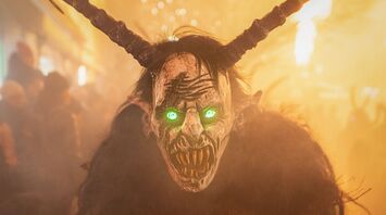 A person dressed as Krampus with glowing green eyes during a festival in Austria