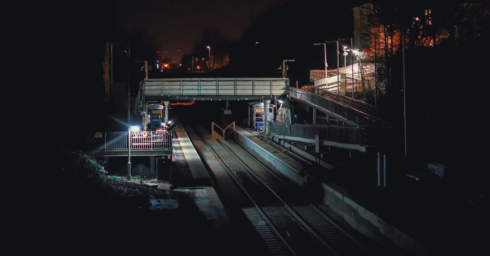 A dimly lit train station at night undergoing repairs with empty tracks and maintenance equipment