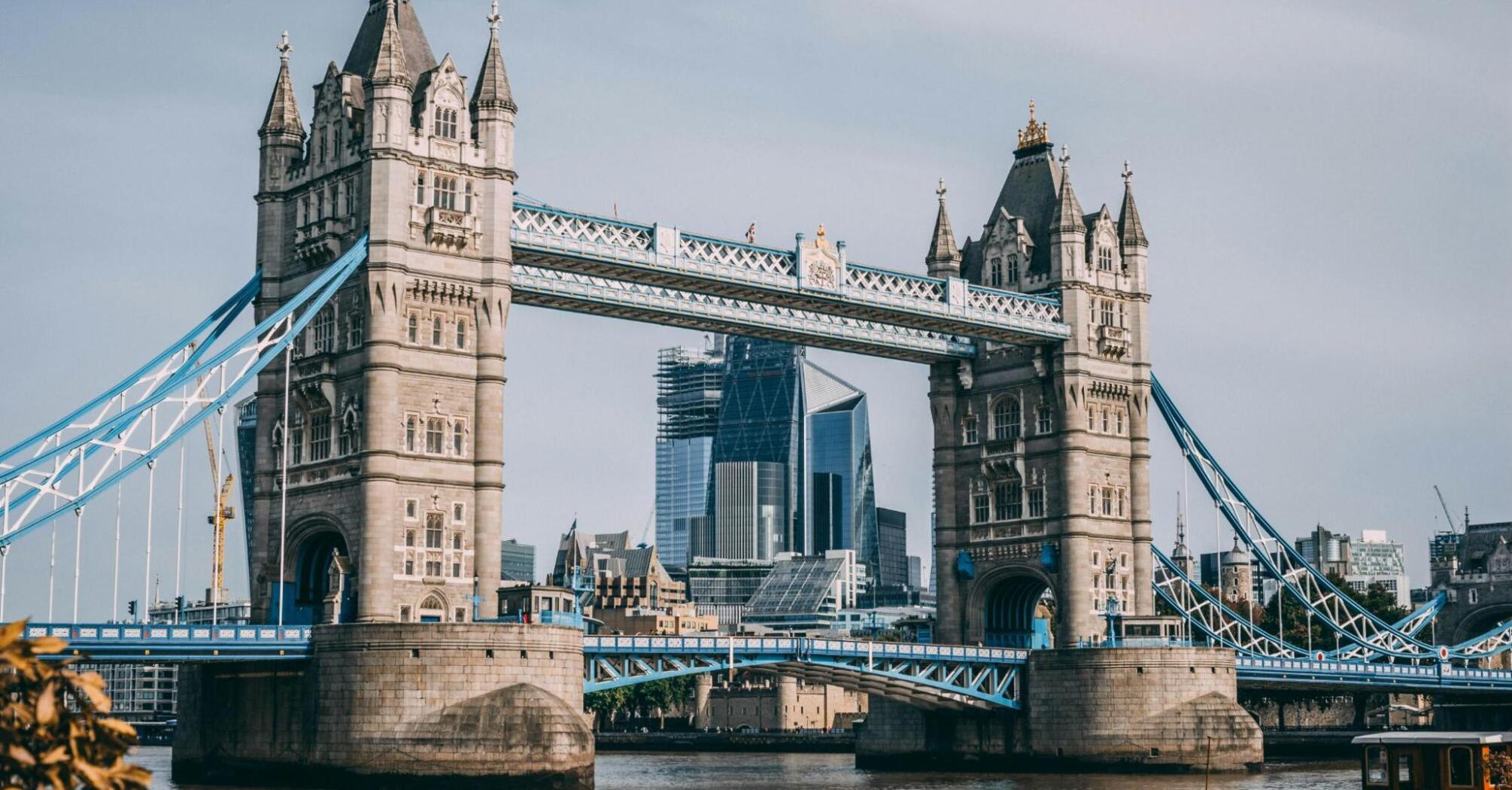 Tower Bridge in London with modern skyscrapers in the background and a boat on the River Thames in the foreground