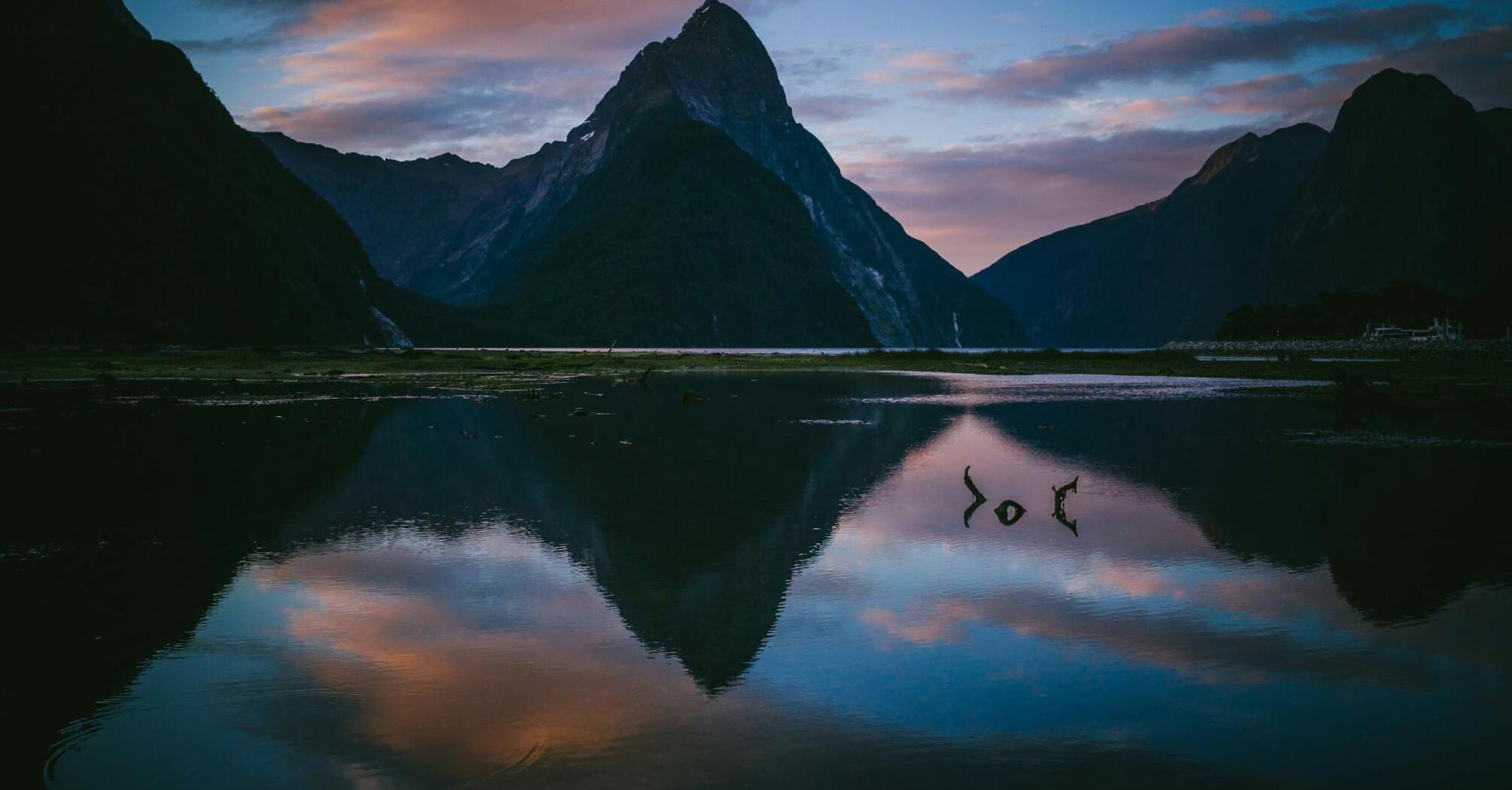 A serene view of Milford Sound at sunset with its reflective waters and towering mountain peaks