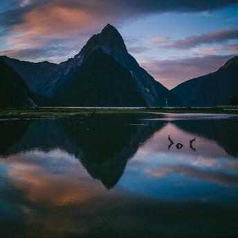 A serene view of Milford Sound at sunset with its reflective waters and towering mountain peaks