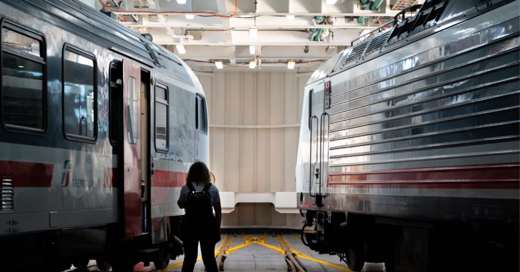 A person standing between two modern Ferrovie Italiane trains in a rail maintenance facility