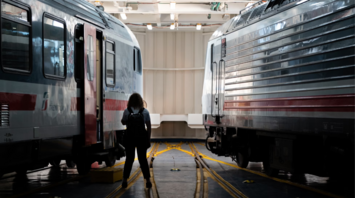 A person standing between two modern Ferrovie Italiane trains in a rail maintenance facility