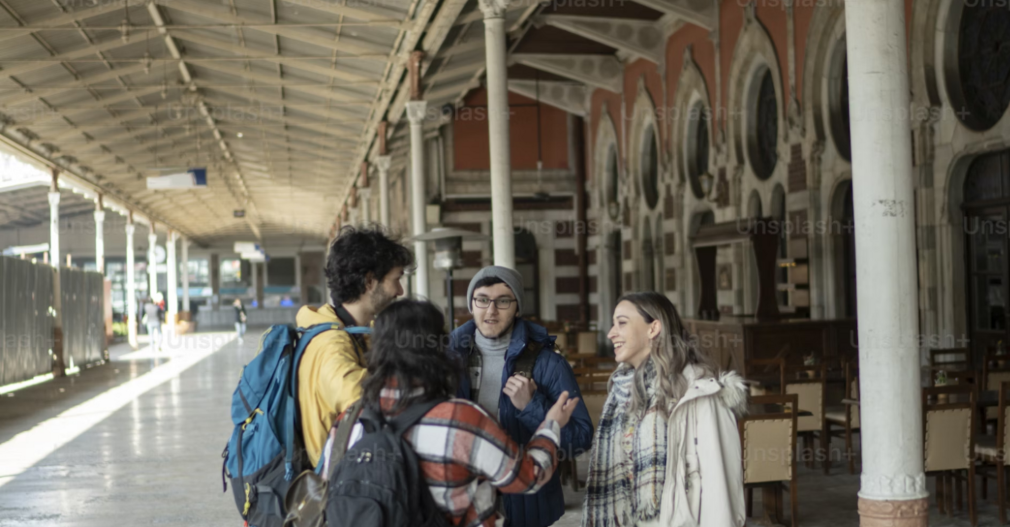 A group of travelers talking under a station clock on a train platform