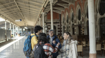 A group of travelers talking under a station clock on a train platform
