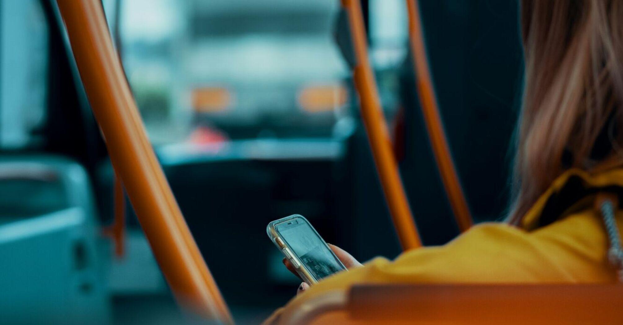 A person sitting on a bus using their phone, surrounded by orange handrails