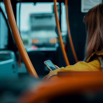 A person sitting on a bus using their phone, surrounded by orange handrails
