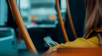 A person sitting on a bus using their phone, surrounded by orange handrails