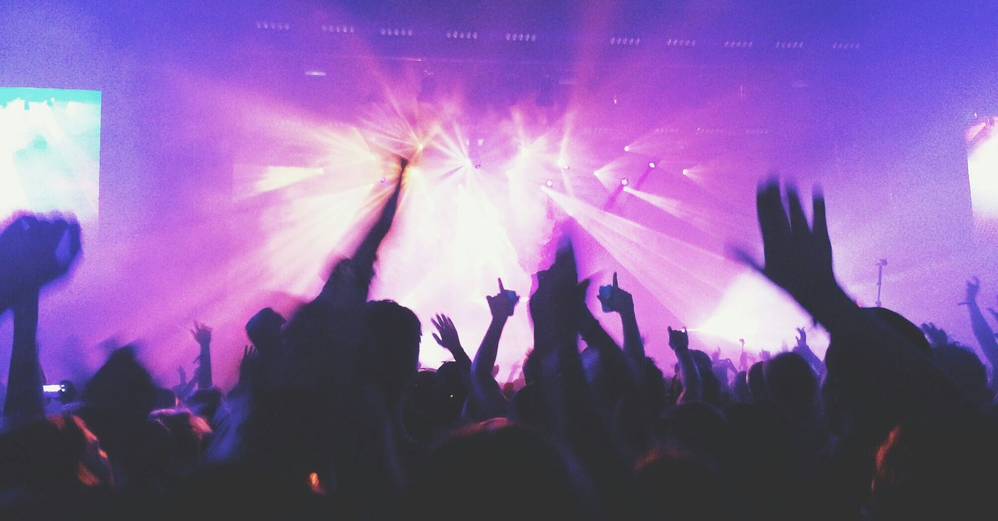 A crowd enjoying a live concert with purple and pink lights illuminating the stage