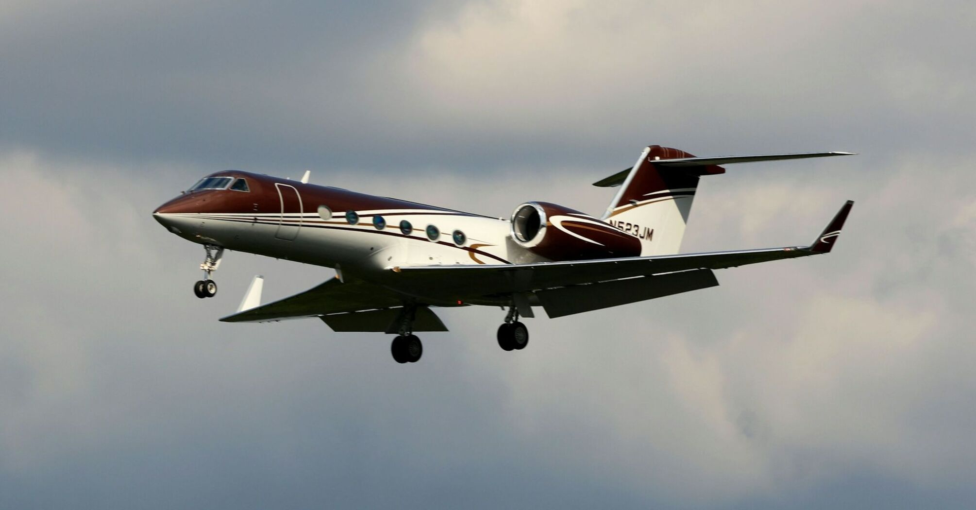 A Gulfstream private jet in flight against a cloudy sky