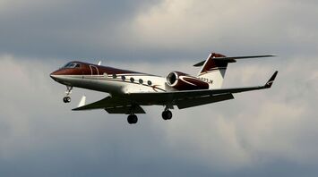 A Gulfstream private jet in flight against a cloudy sky