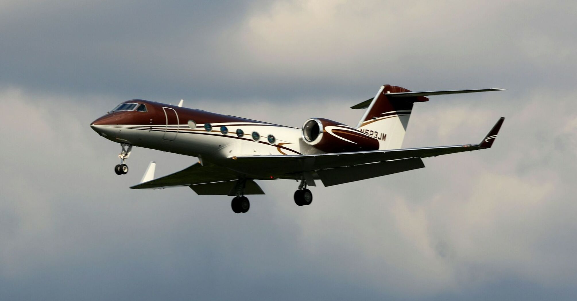 A Gulfstream private jet in flight against a cloudy sky