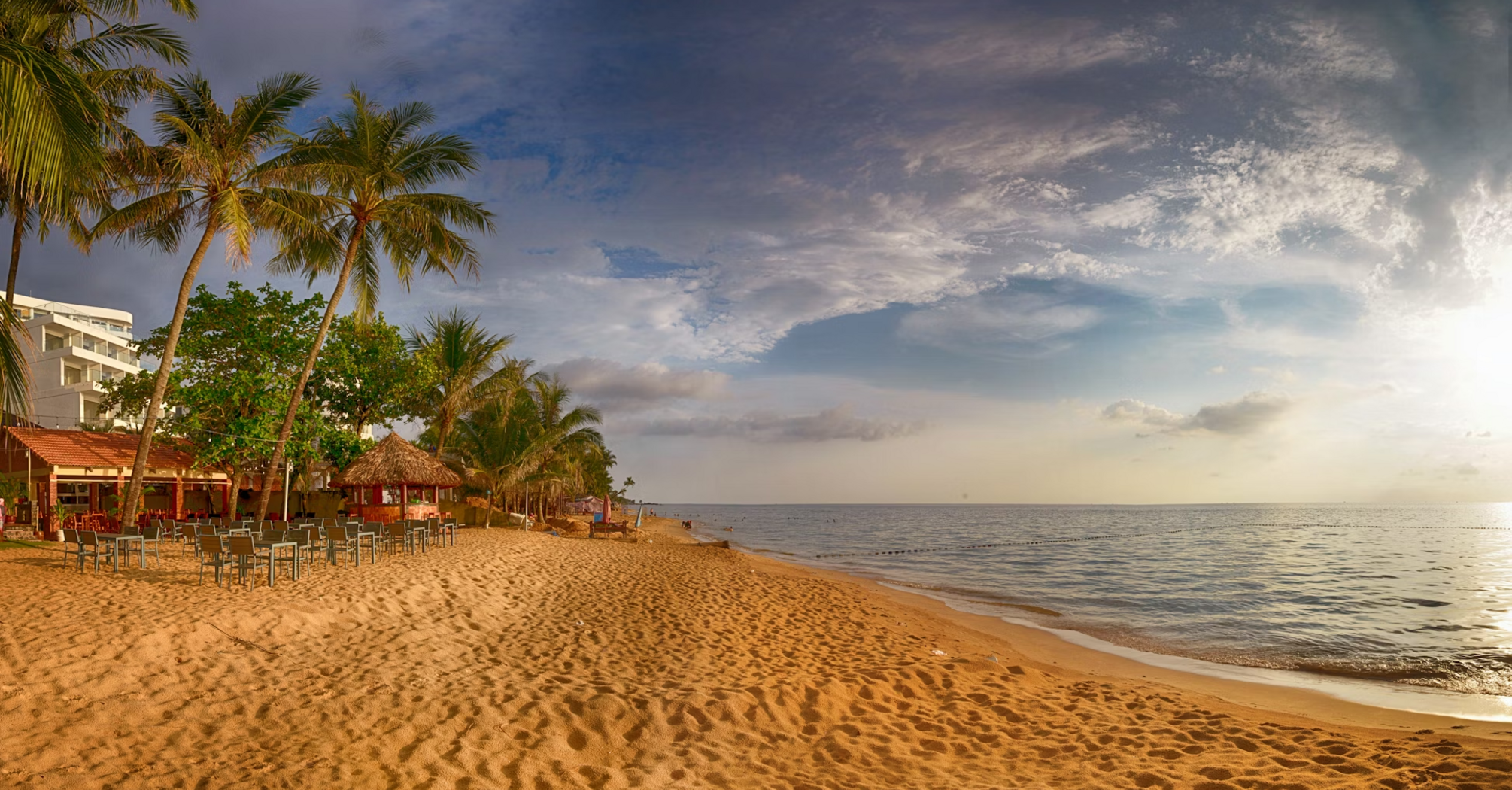 A serene tropical beach with palm trees and outdoor seating during sunset