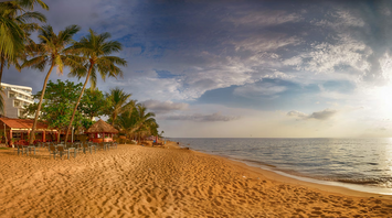 A serene tropical beach with palm trees and outdoor seating during sunset