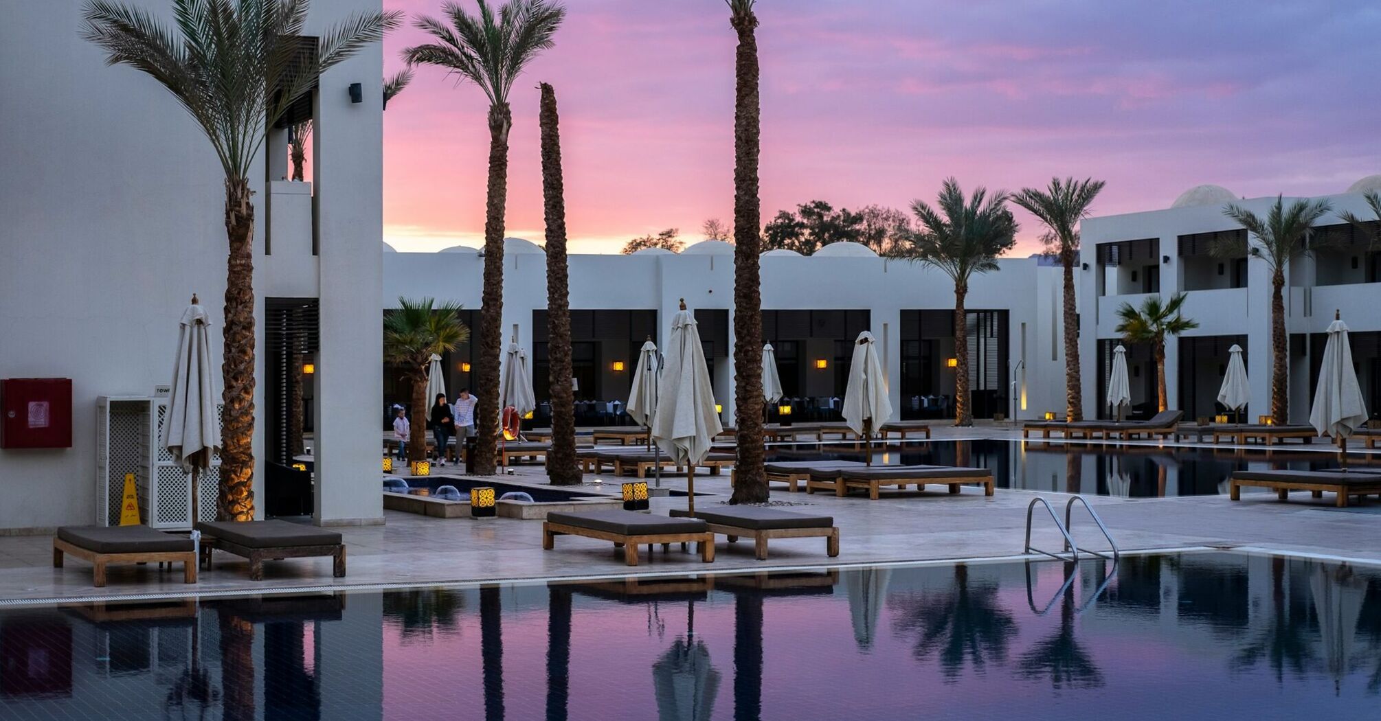 A luxurious resort pool surrounded by palm trees at sunset