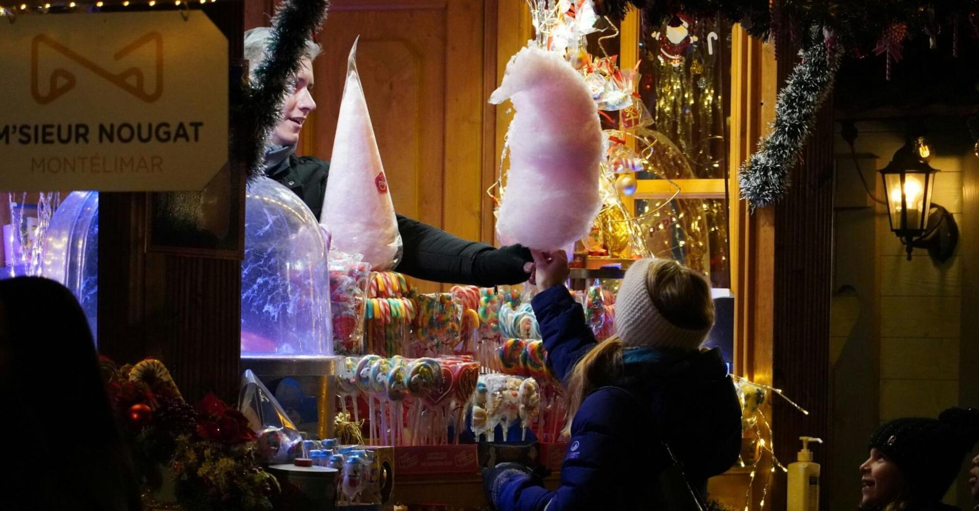 A festive market stall offering cotton candy and colorful sweets, surrounded by warm lights and holiday decorations