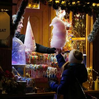 A festive market stall offering cotton candy and colorful sweets, surrounded by warm lights and holiday decorations
