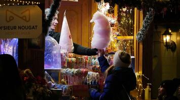 A festive market stall offering cotton candy and colorful sweets, surrounded by warm lights and holiday decorations
