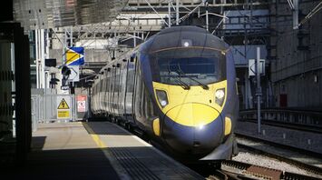 A modern train arriving at a platform under a bright sky with visible overhead electric line