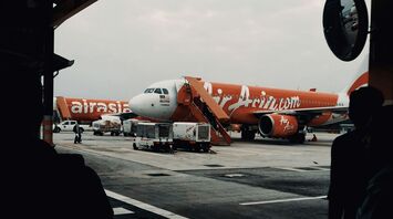 An AirAsia airplane parked at the airport tarmac with a mobile staircase in front for boarding