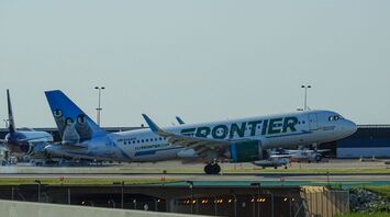 Frontier Airlines aircraft parked at an airport runway with penguin artwork on its tail