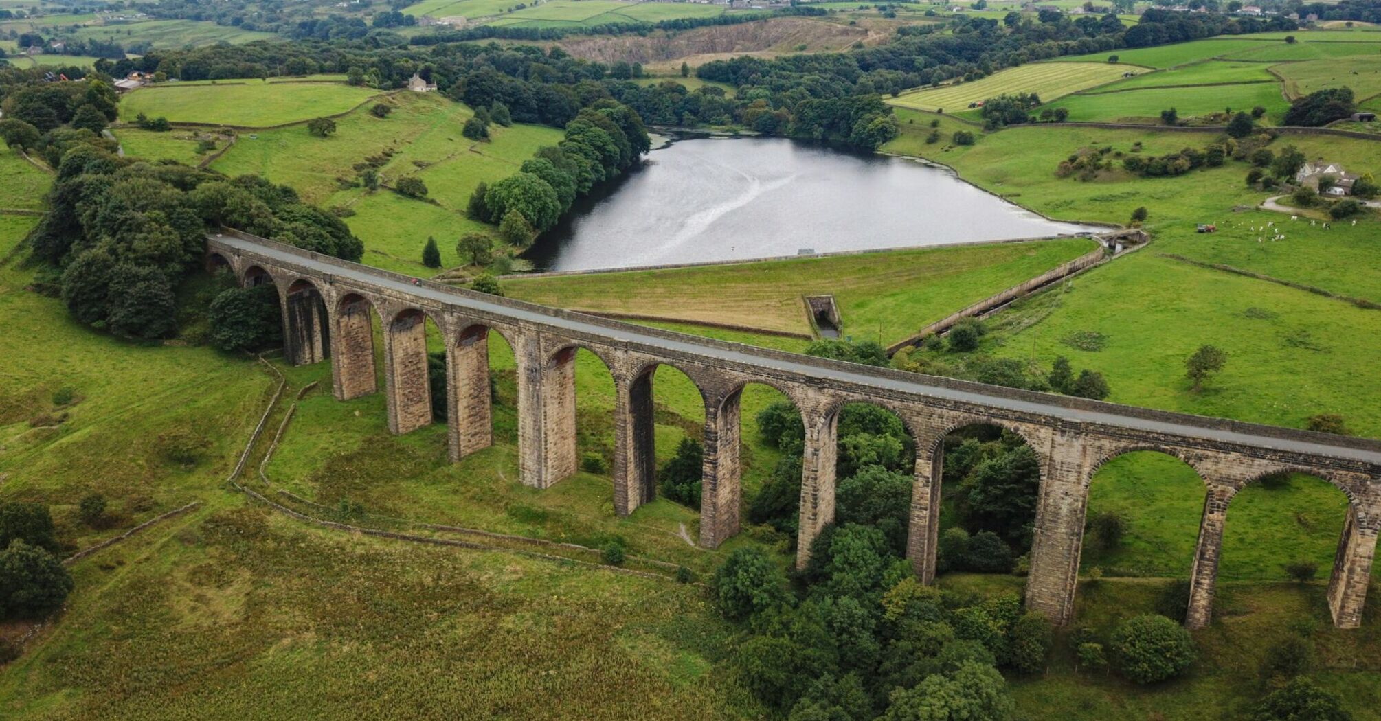 A historic railway viaduct stretching across lush green hills with a reservoir in the background